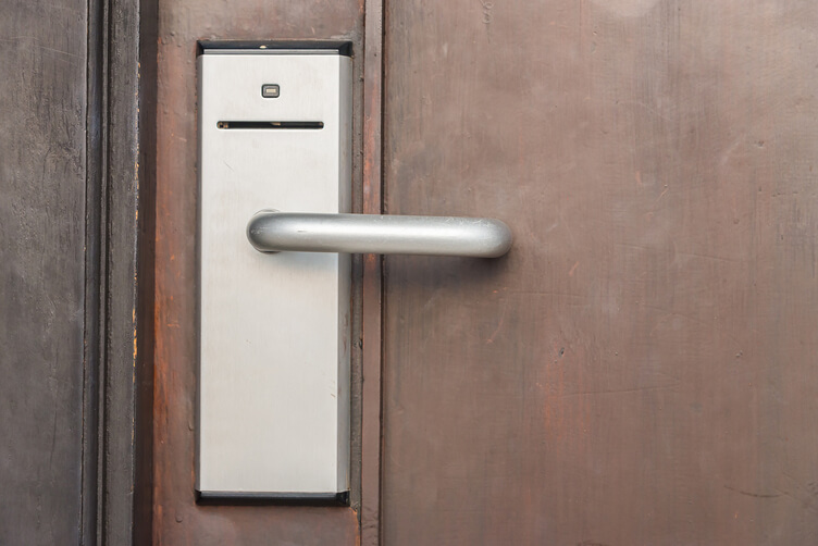 Electronic hotel key card door lock with slot reader and silver lever handle on brown wooden door for secure access.